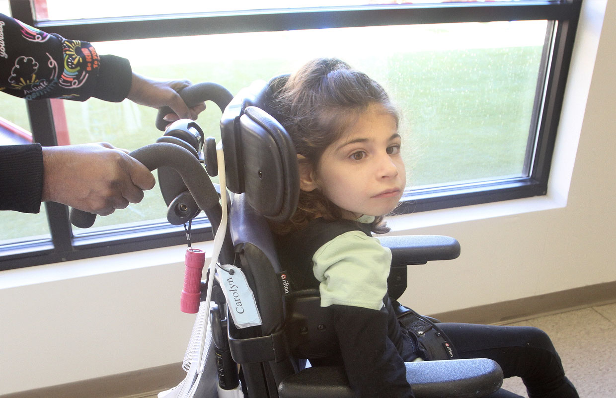 Female elementary student using wheelchair Assistive Technology in hallway with teacher