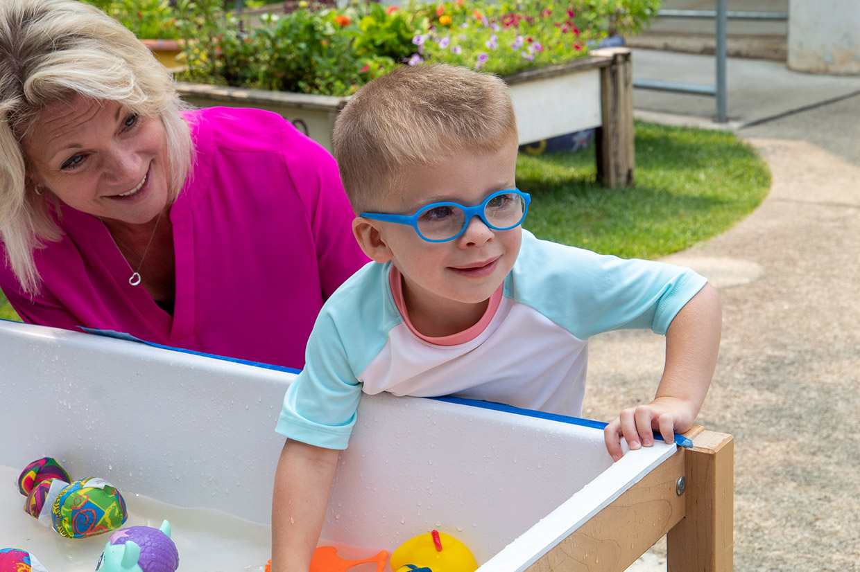 P.G. Chambers School male preschool student smiling and playing in an outdoor water table.
