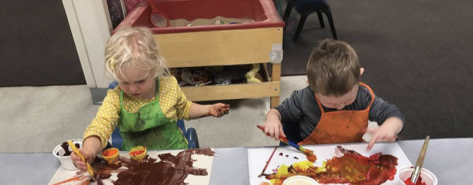 One female and one male preschool students painting together at a school table